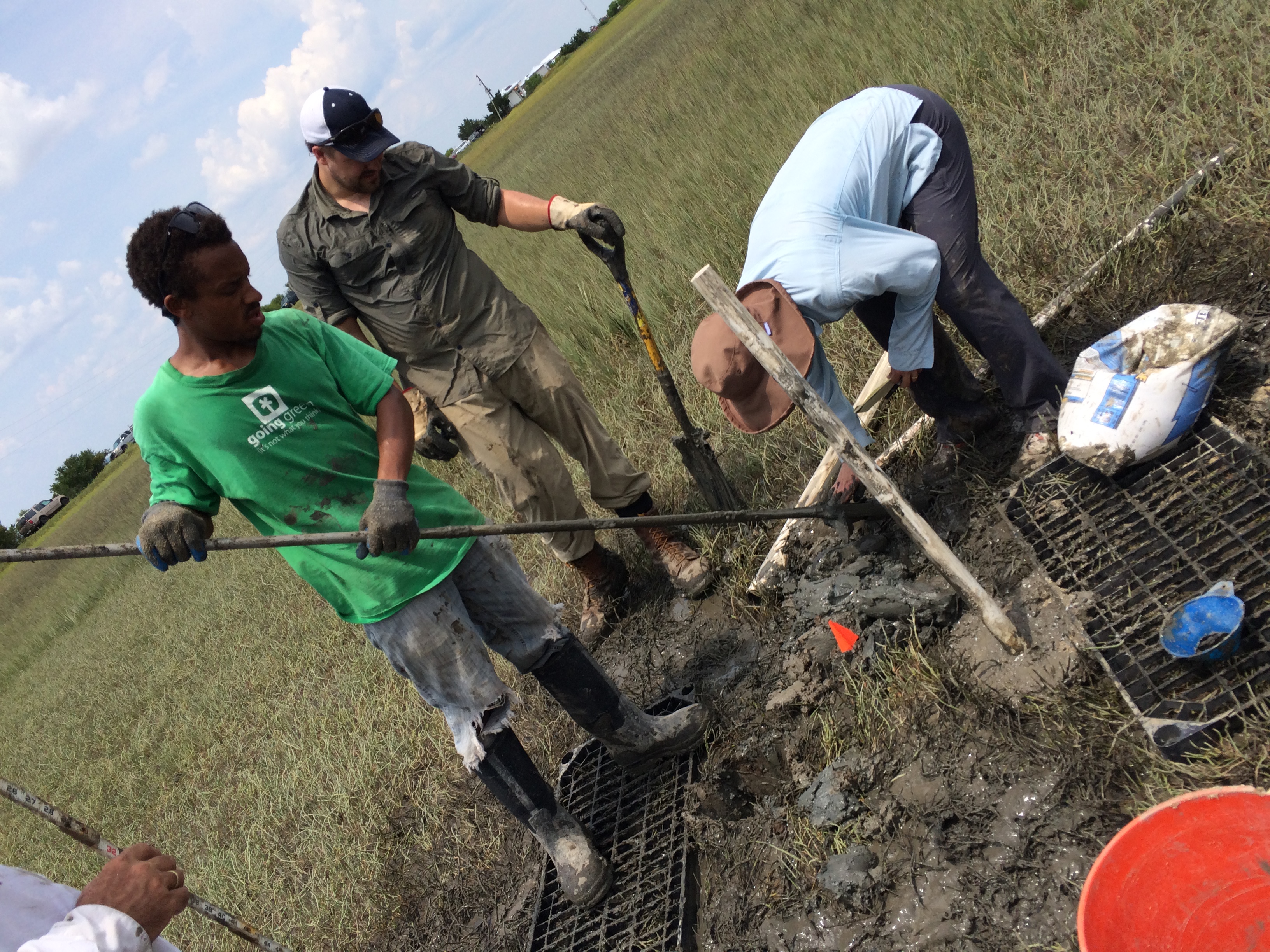 Three people installing a well in a salt marsh